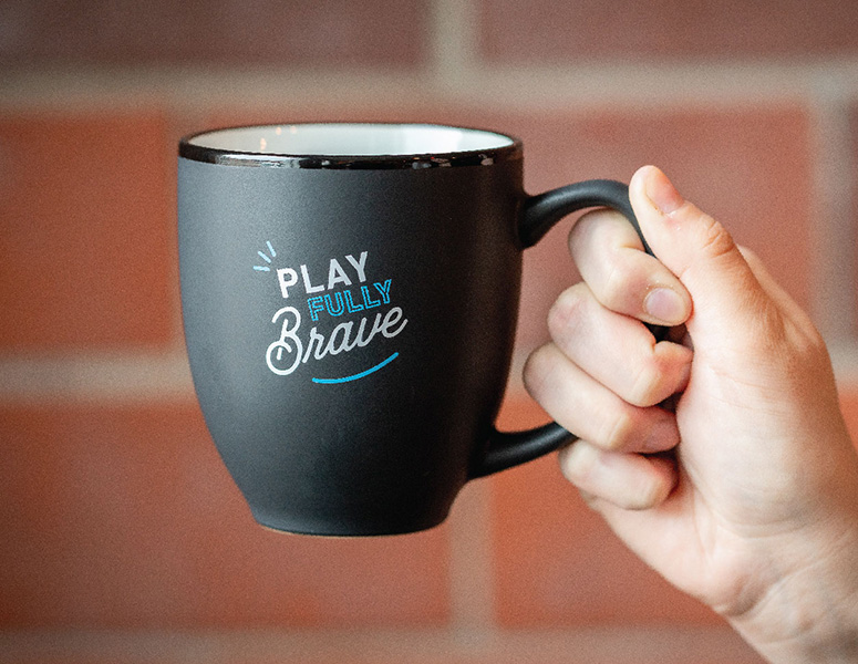 Black mug with white and blue text that reads "Play Fully Brave"