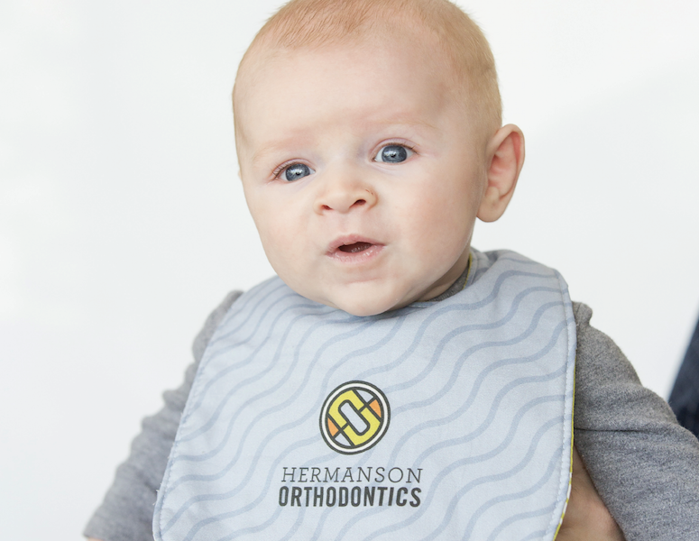 Baby wearing a bib with the Hermanson Orthodontics logo