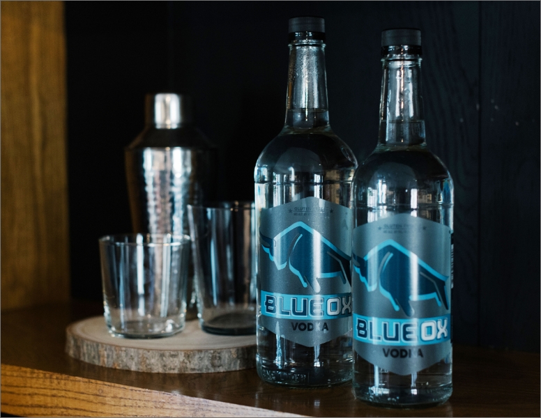 Two bottles of Blue Ox Vodka on a home shelf with glasses and a cocktail shaker