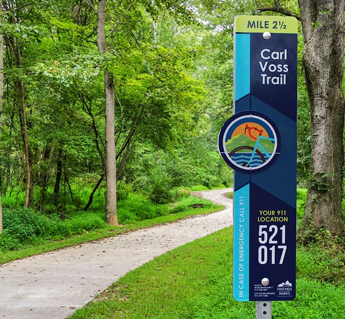 Carl Voss Trail E-911 sign amidst green trees beside a paved trail